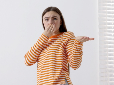 Person in striped orange and white shirt covering nose with one hand and gesturing with the other, expressing concern about a strong burning odor, indicative of potential furnace overheating issues.